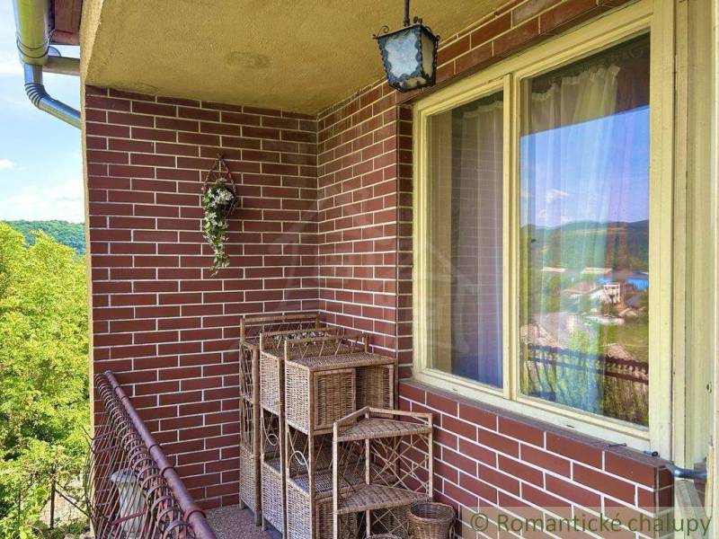 A brick balcony of a family house in Gemerská Hôrka with hanging flowers and a view.