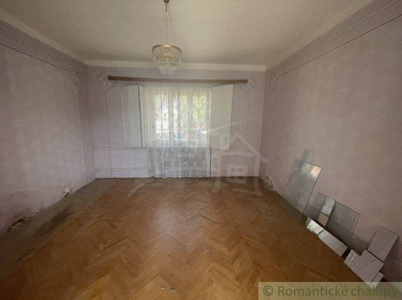 A room in a family house with a parquet floor, a chandelier, and lace curtains.