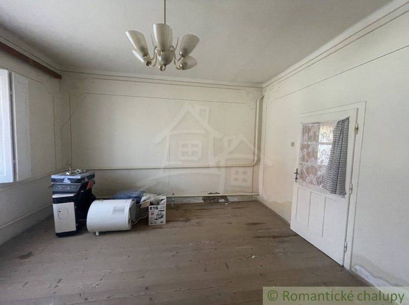 A room in a family house with a wooden floor, a chandelier, and white walls.