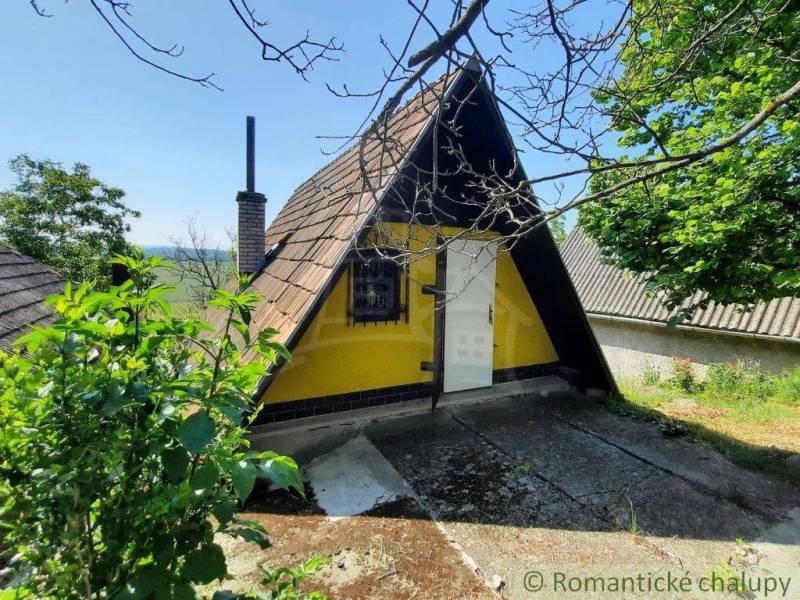 Yellow cottage in Malé Kozmálovce with a triangular roof, surrounded by greenery.