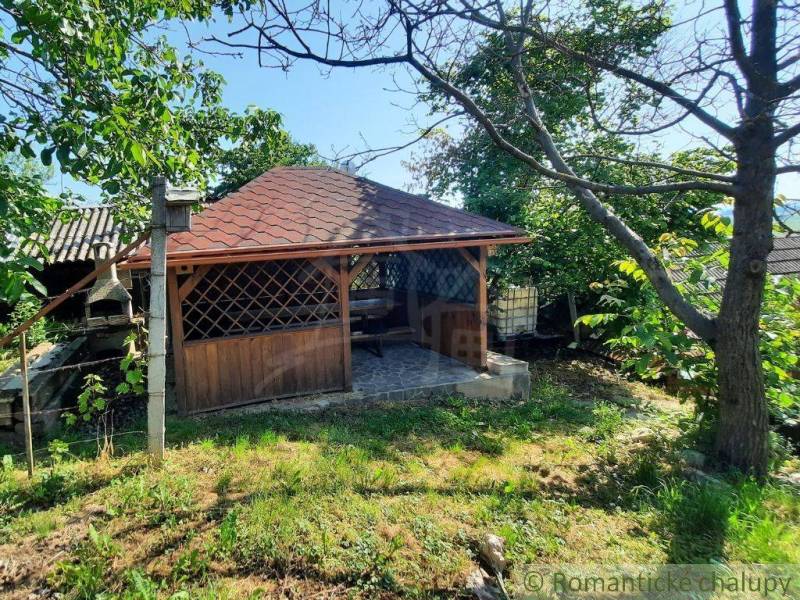 A wooden gazebo near the cottage in Malé Kozmálovce is surrounded by green trees and lawn.