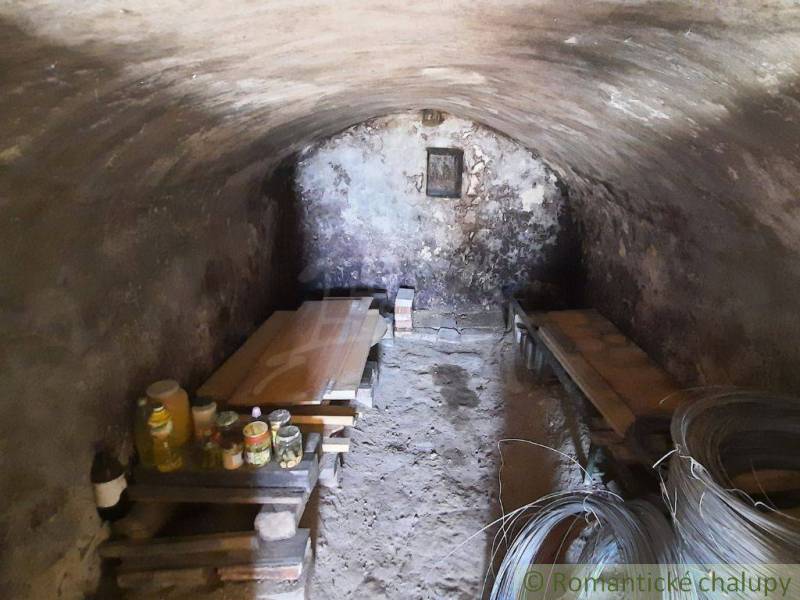 Stone cellar in a cottage with wooden benches and canned goods for storage.