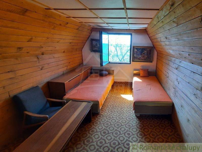 Wooden paneling, two beds, an armchair, and a table in an attic room in a cottage.
