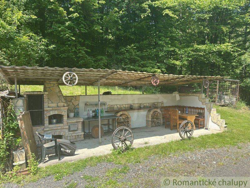Covered garden seating area at a family house in Poltár with a stone fireplace and wooden decorations.