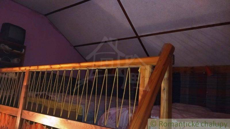 Attic in a cottage with wooden railing, bed, and television.