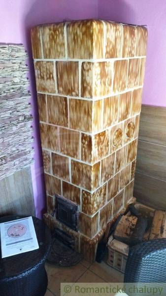 A tiled stove in a cabin with wooden details and a table in a cozy corner.