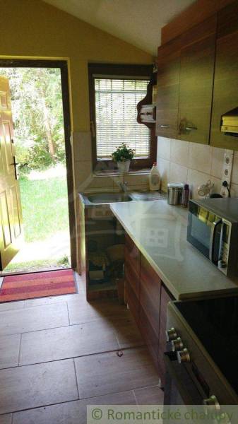A kitchen in a cottage with a garden view, featuring wooden furniture and ceramic tiles.