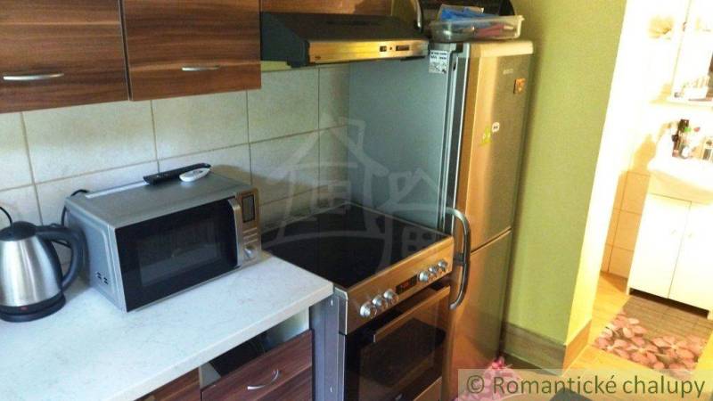 A kitchen in a cottage with a microwave, electric kettle, and stove, next to a refrigerator.