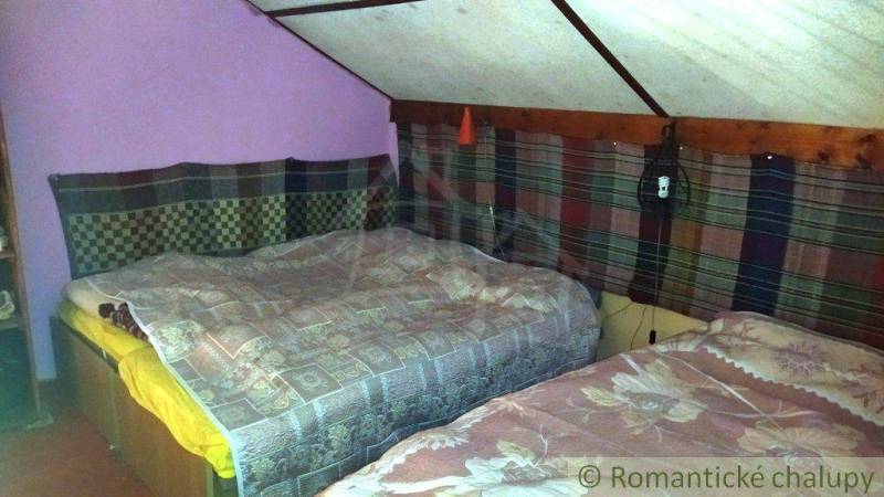 Two beds in the attic of the cottage with colorful textiles on the walls.