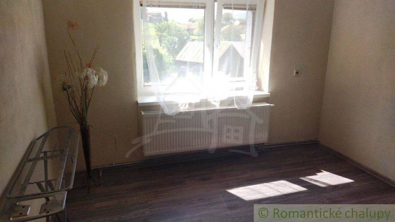 A room with a large window, wooden floor, and floral decoration in a family house.