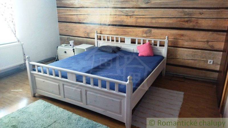 Bedroom in a family house with a wooden wall and a white bed.