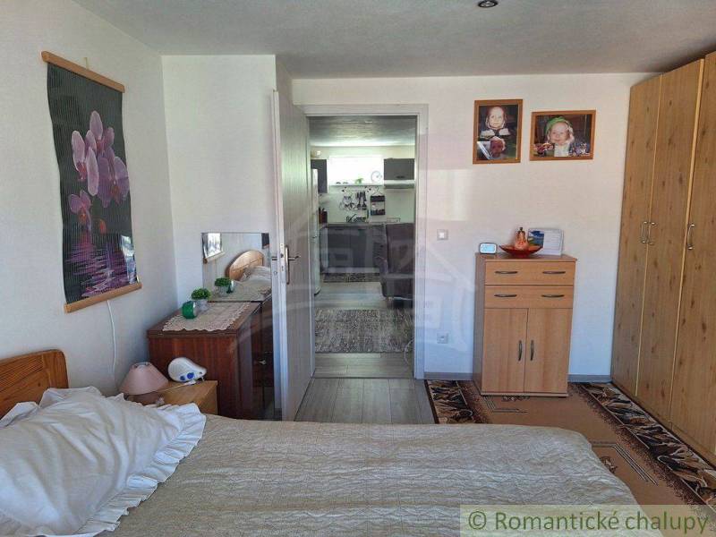 A bedroom in a family house with furniture and decorations, visible hallway and part of the kitchen.