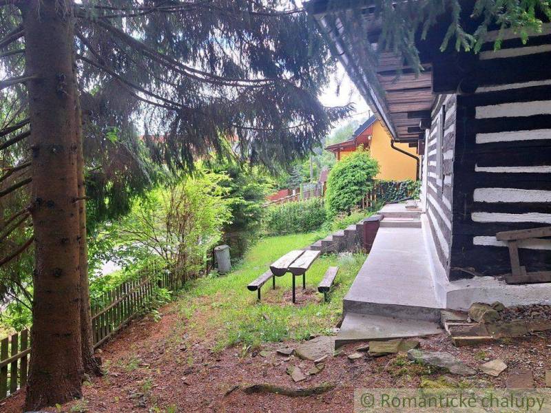 A family house in Ružomberok with wooden walls, a bench, and a garden surrounded by trees.