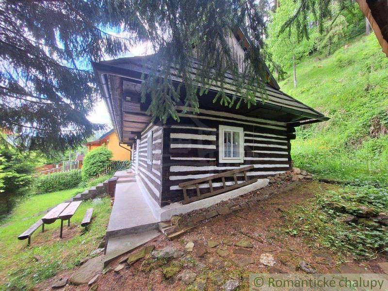 A wooden family house in Ružomberok surrounded by greenery, with a bench and a table in the garden.