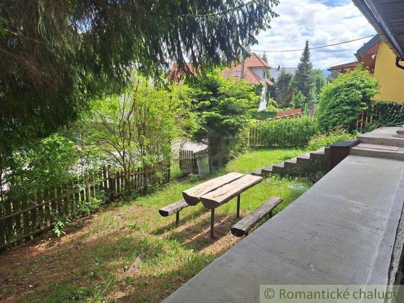 A garden with a bench and a table by a family house in Ružomberok, surrounded by greenery.