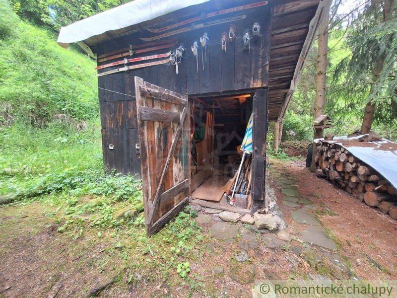 A shed by a family house in Ružomberok, surrounded by shelters and wood in a forest area.