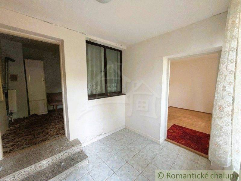 A hallway of a family house with tiles, carpet, and a view into two rooms.