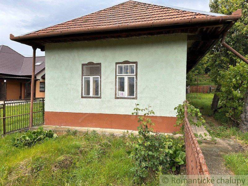 A cottage in Nové Zámky with a green facade and a sloped roof, surrounded by greenery.