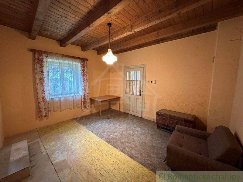 The interior of a cabin with a wooden ceiling, a couch, and a table next to a window with floral curtains.
