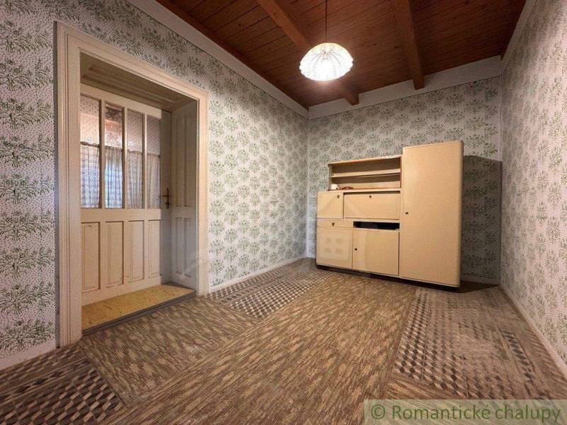 The interior of a cabin with a wooden ceiling, floral wallpaper, and vintage furniture.