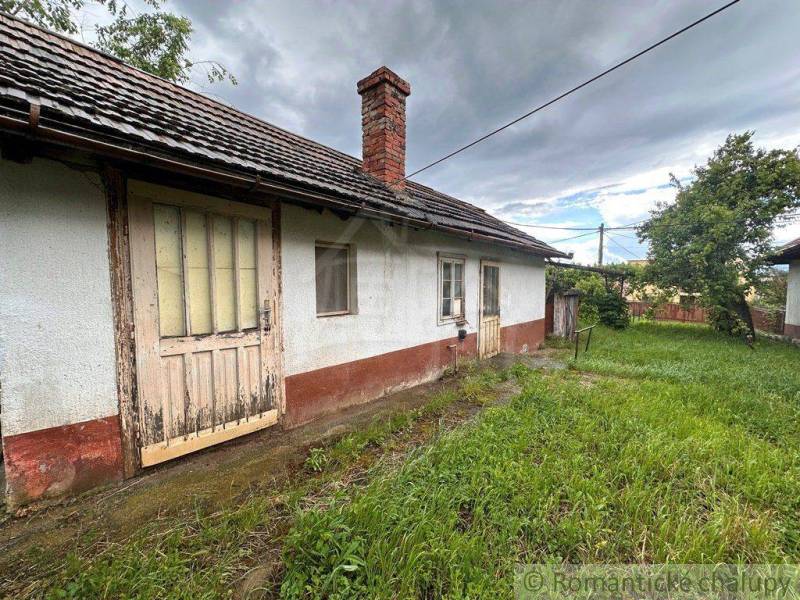 An older cottage in Nové Zámky with wooden doors and a grassy yard.
