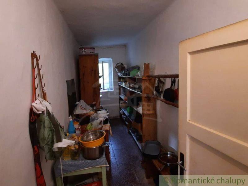 A narrow room with old furniture and shelves in a family house, with a door at the front.