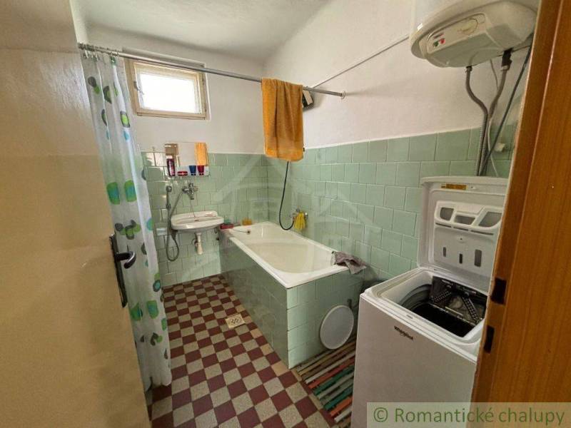 A bathroom in a family house with a bathtub, washing machine, and green tiles.