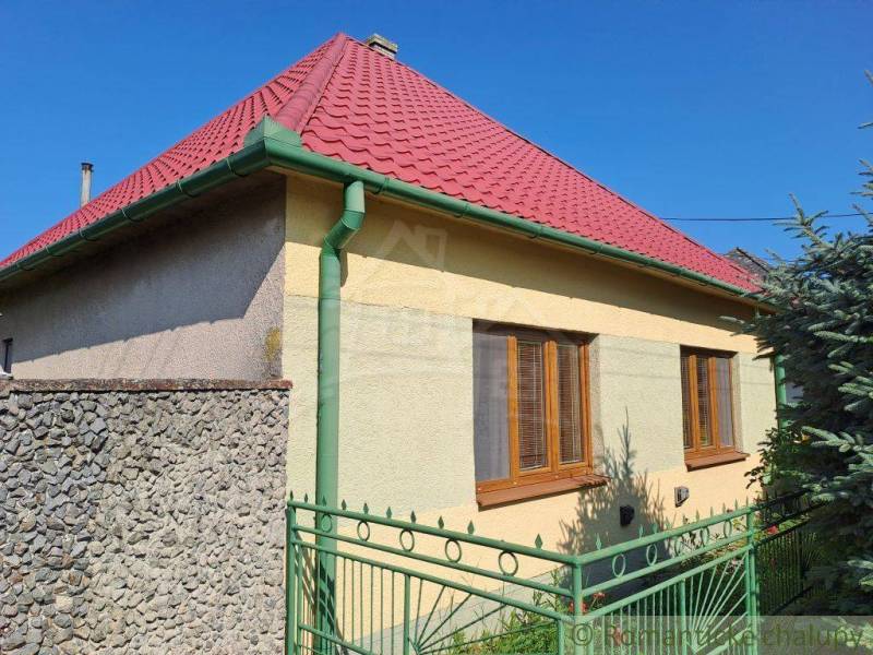 A family house in Dvorníky with a sloped roof, a green fence, and windows on the sunny side.