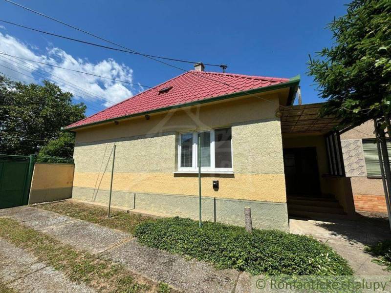 A family house in Dvorníky with a red roof and a green gate, part of the facade is yellow.