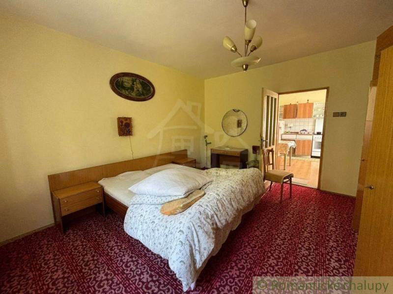 A bedroom with a bed, a mirror, and open doors leading to the kitchen in a family house.