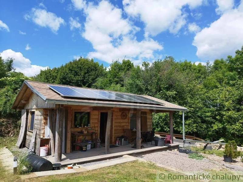 A wooden cabin with photovoltaic panels in nature near Veľký Krtíš under a blue sky.