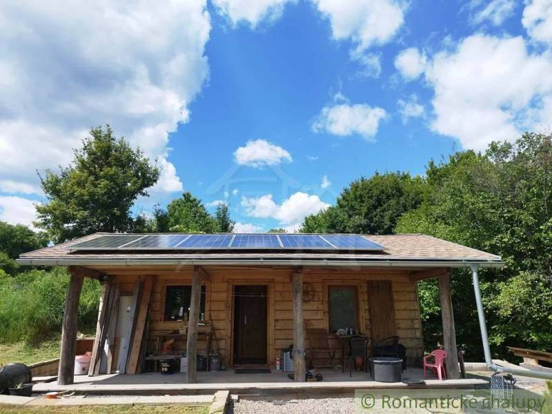 A wooden cabin in Veľký Krtíš with solar panels surrounded by nature and a blue sky.