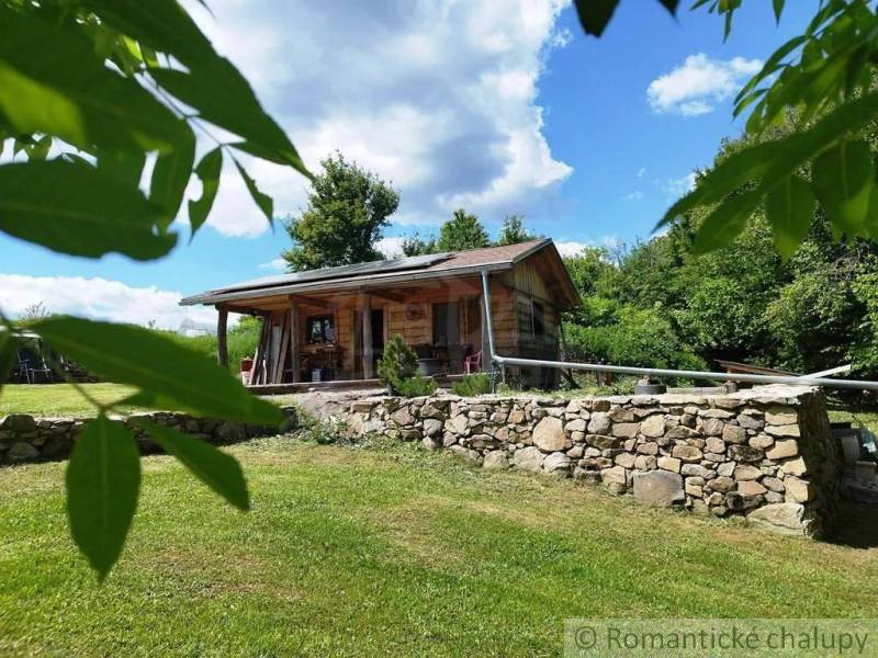 A wooden cottage in Veľký Krtíš surrounded by greenery and a stone wall.