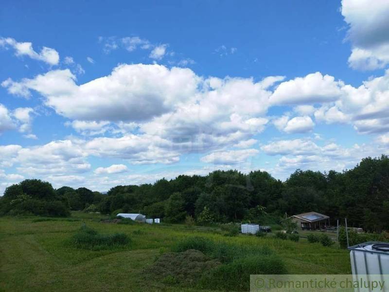 A cottage near Veľký Krtíš surrounded by a green meadow and a blue sky.
