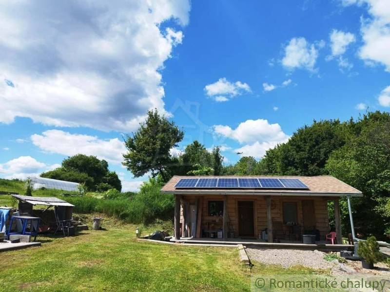 A cottage in Veľký Krtíš with a lawn and solar panels, surrounded by greenery and a blue sky.