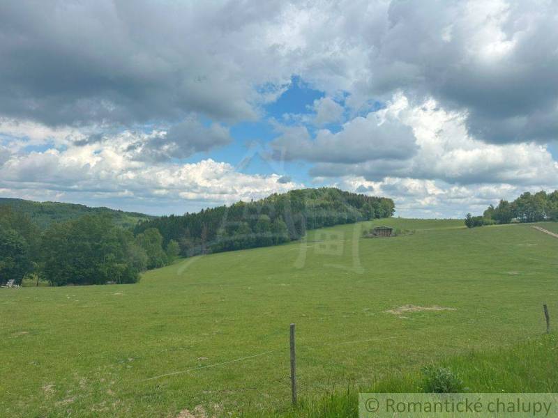 Green meadows and hills under a cloudy blue sky in the Gardens in České Brezové.