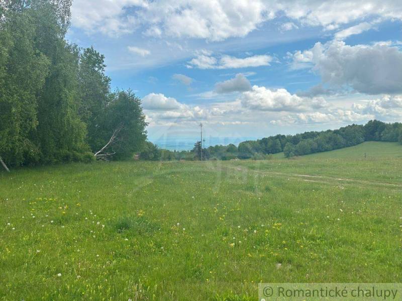 Gardens in České Brezová display green meadows, trees, and a blue sky with clouds.