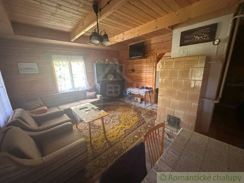 Interior of a cabin with wooden paneling, rustic furniture, and a stove for heating.
