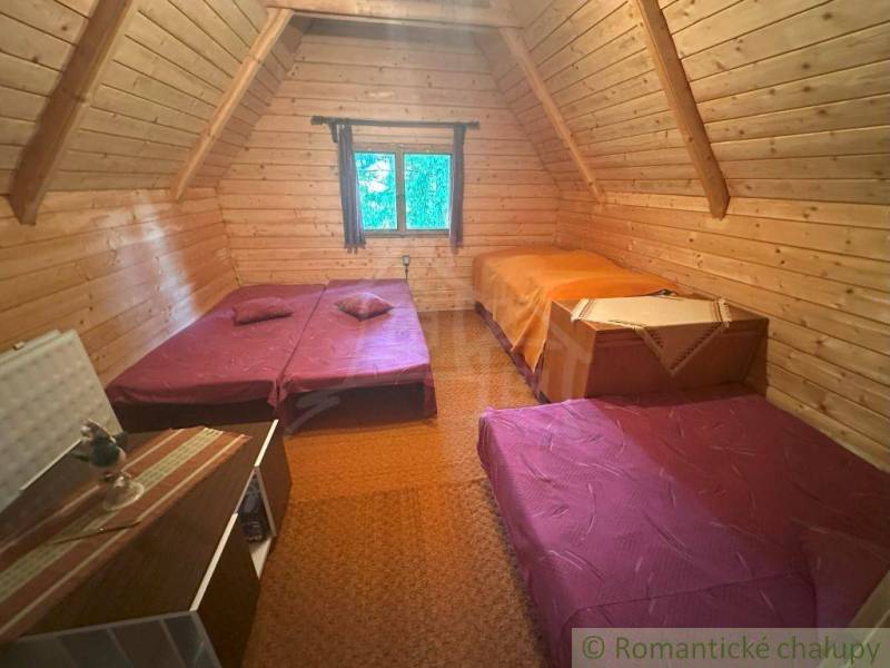 Attic room in a cabin with wooden walls and three beds.