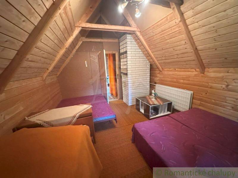 Attic room in a cabin with a slanted wooden ceiling, two beds, and a table.