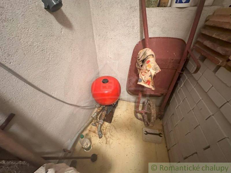 Workshop pit on a cottage with a wheelbarrow and a red expansion tank.