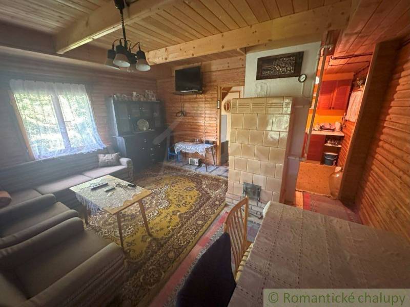A wooden interior of a cabin with a tiled stove and a living area.