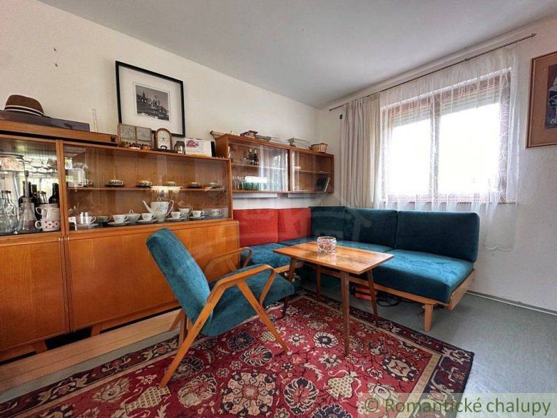 The interior of a cabin with retro furniture, a carpet, a sofa, and a display cabinet with cups.