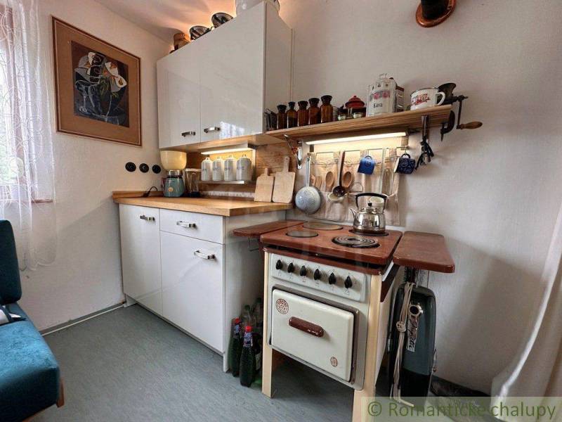A cottage kitchen with a retro stove, a shelf, and a variety of kitchen accessories.