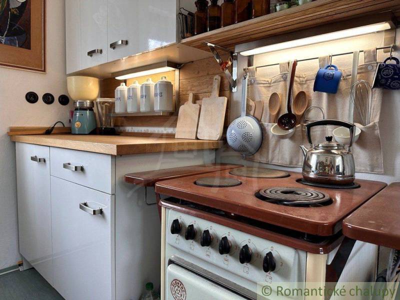 A kitchen in a cottage with wooden details, an old stove, and hanging utensils.