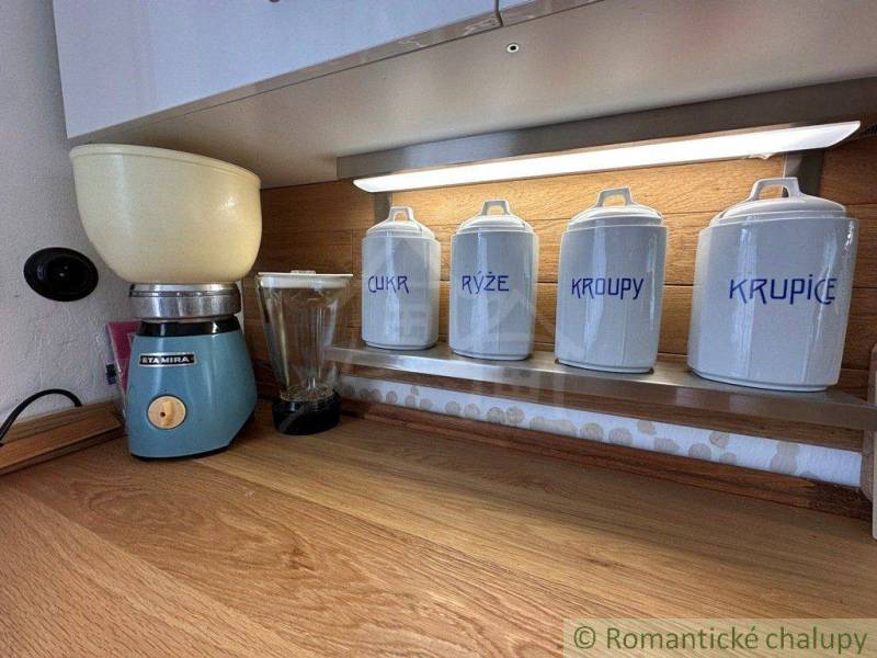 The kitchen shelf of the cottage with jars for sugar, rice, groats, semolina, and a grinder.