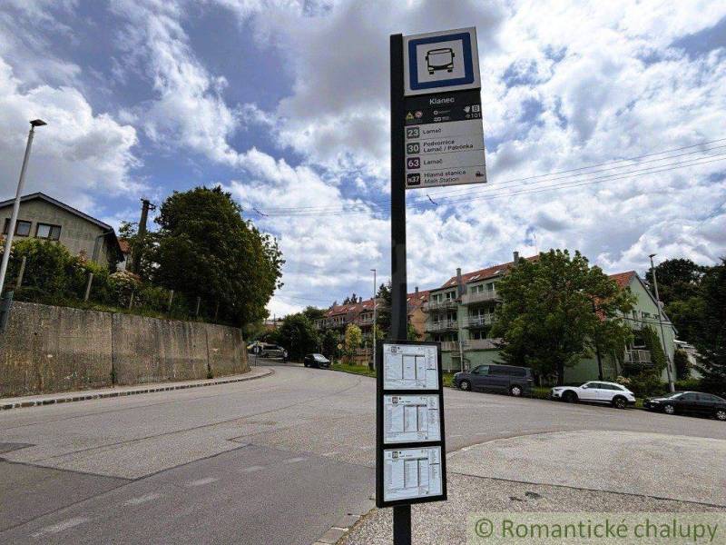 Bus stop in Bratislava-Lamač, surrounded by residential buildings and green trees.
