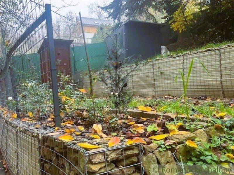A cottage in Bratislava - Lamač with a terraced garden, gabion fence, and leaves on the ground.