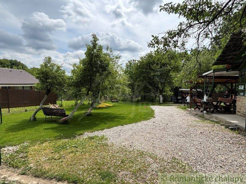 The garden of the cottage in Bratislava-Lamač with benches, trees, and a gravel path.