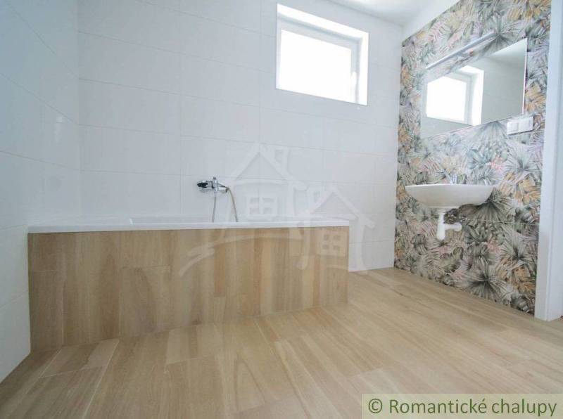 A bathroom in a family house with a bathtub and a sink, light tiles, plant-patterned tiles.